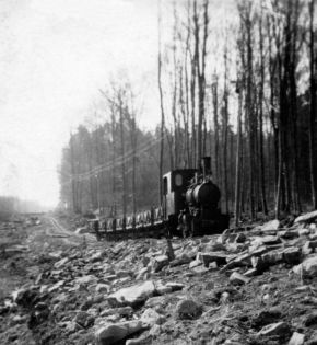 Das schwarzweiß Foto zeigt eine Dampflokomotive mit Muldenkipper.